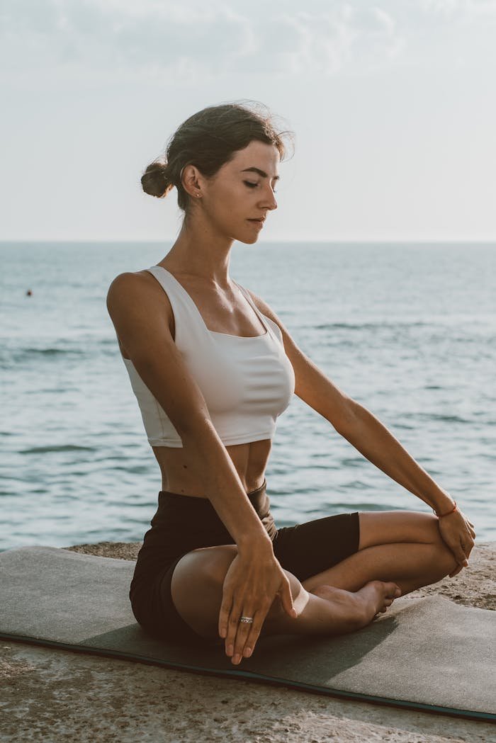 Adult woman practicing meditation on a yoga mat by the sea, enjoying calmness outdoors.