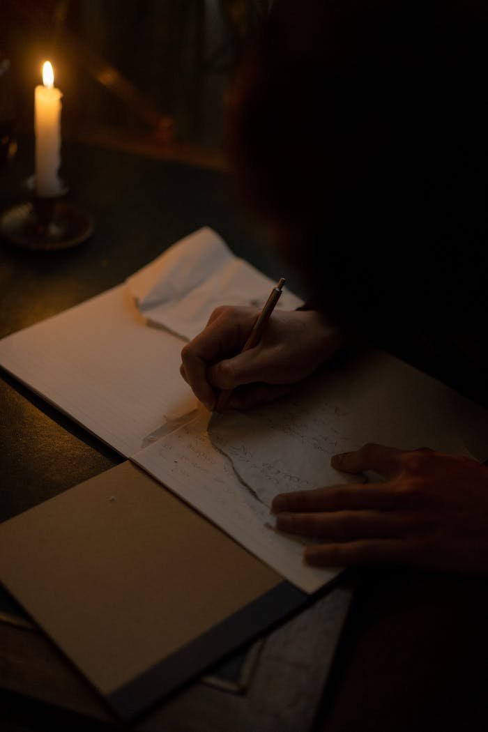 A person writes in a notebook by candlelight creating a dark and focused atmosphere.